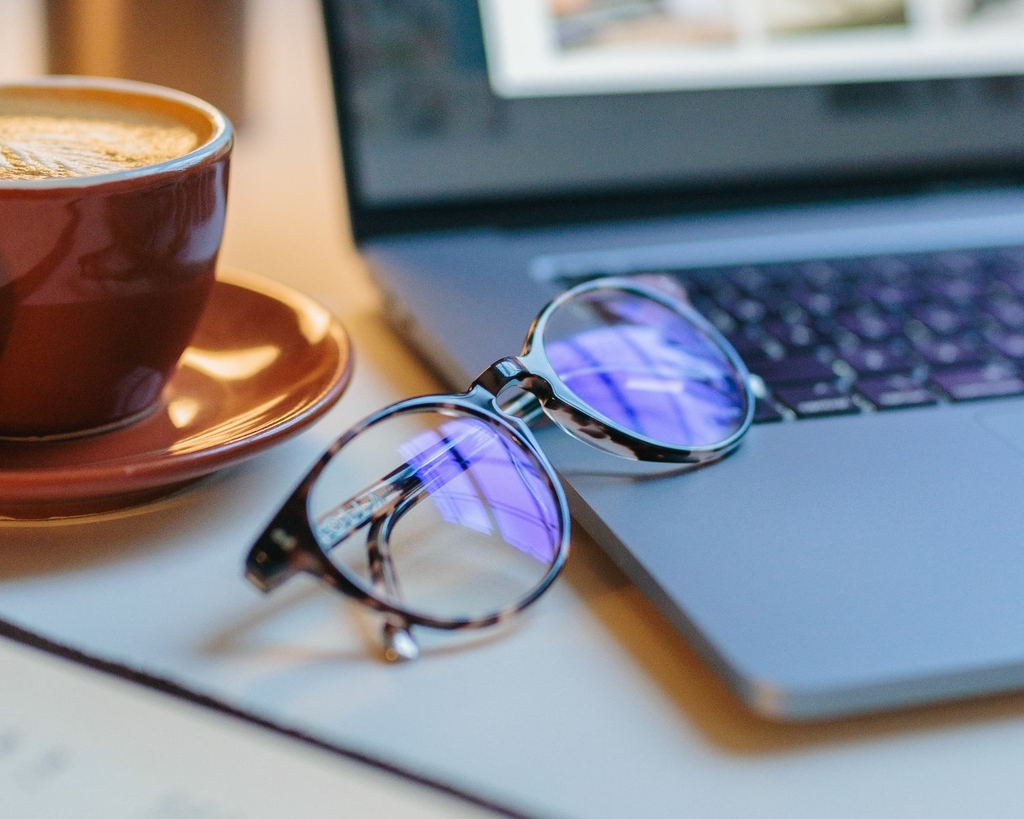 Blue light filter glasses resting on a laptop beside a coffee