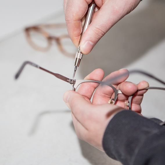 Frame being held in a hand and a screwdriver tightening the glasses frame