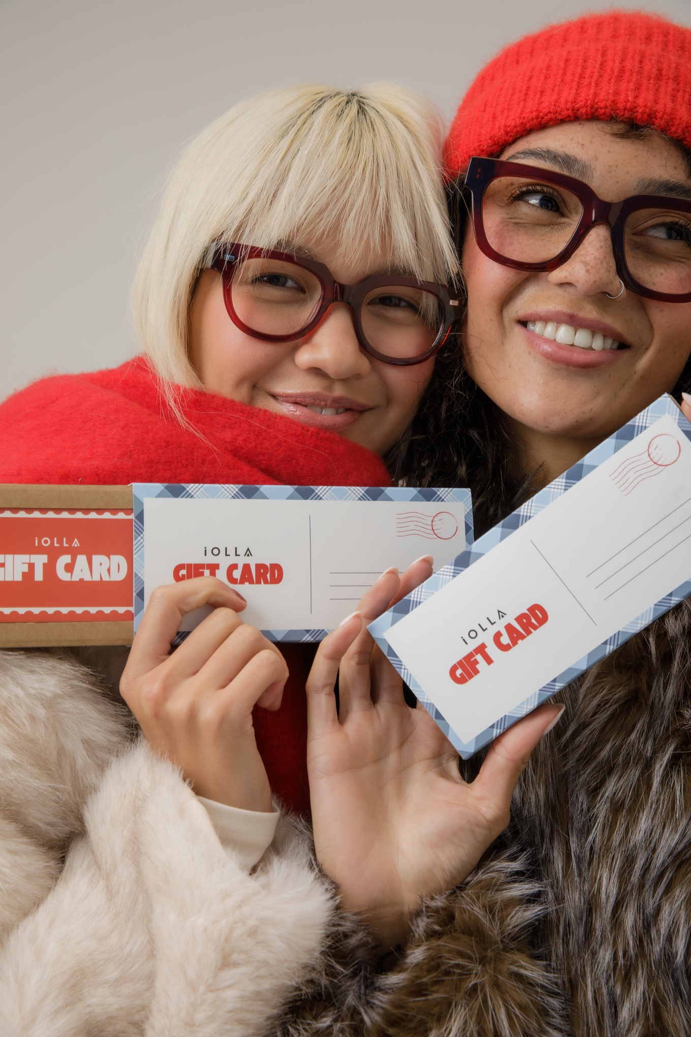 Two friends in IOLLA glasses holding IOLLA Christmas gift cards in festive sleeves